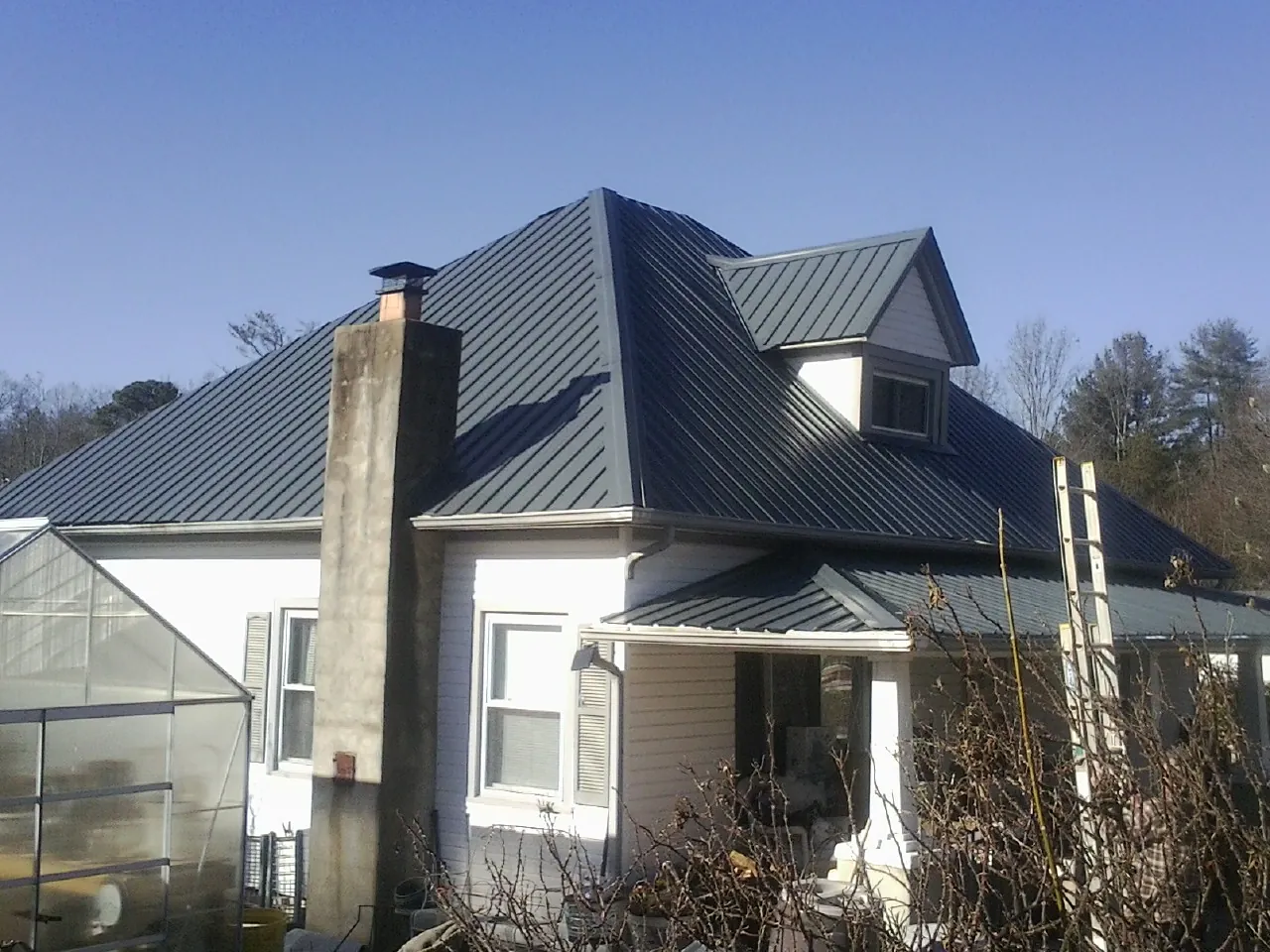 Dark blue standing seam metal roof on a white farmhouse with dormer — Slate & Tile Roof Repair by Roofing Brothers in Romney