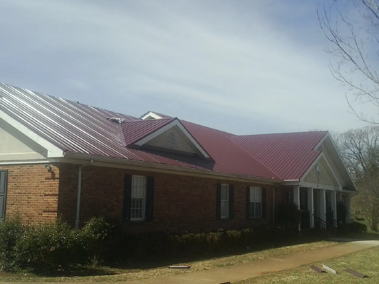 Red metal roof with gabled entries on a long brick building, from a Hail Damage Roof Repair job in Romney