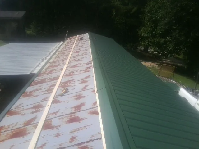 Old rusted panels beside newly installed green metal roofing — Wind Damage Roof Repair by Roofing Brothers in Romney