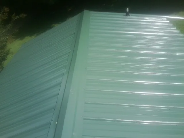 New green metal panels meeting at the ridge of a roof — Flat Roof Repair work by our crew in Romney