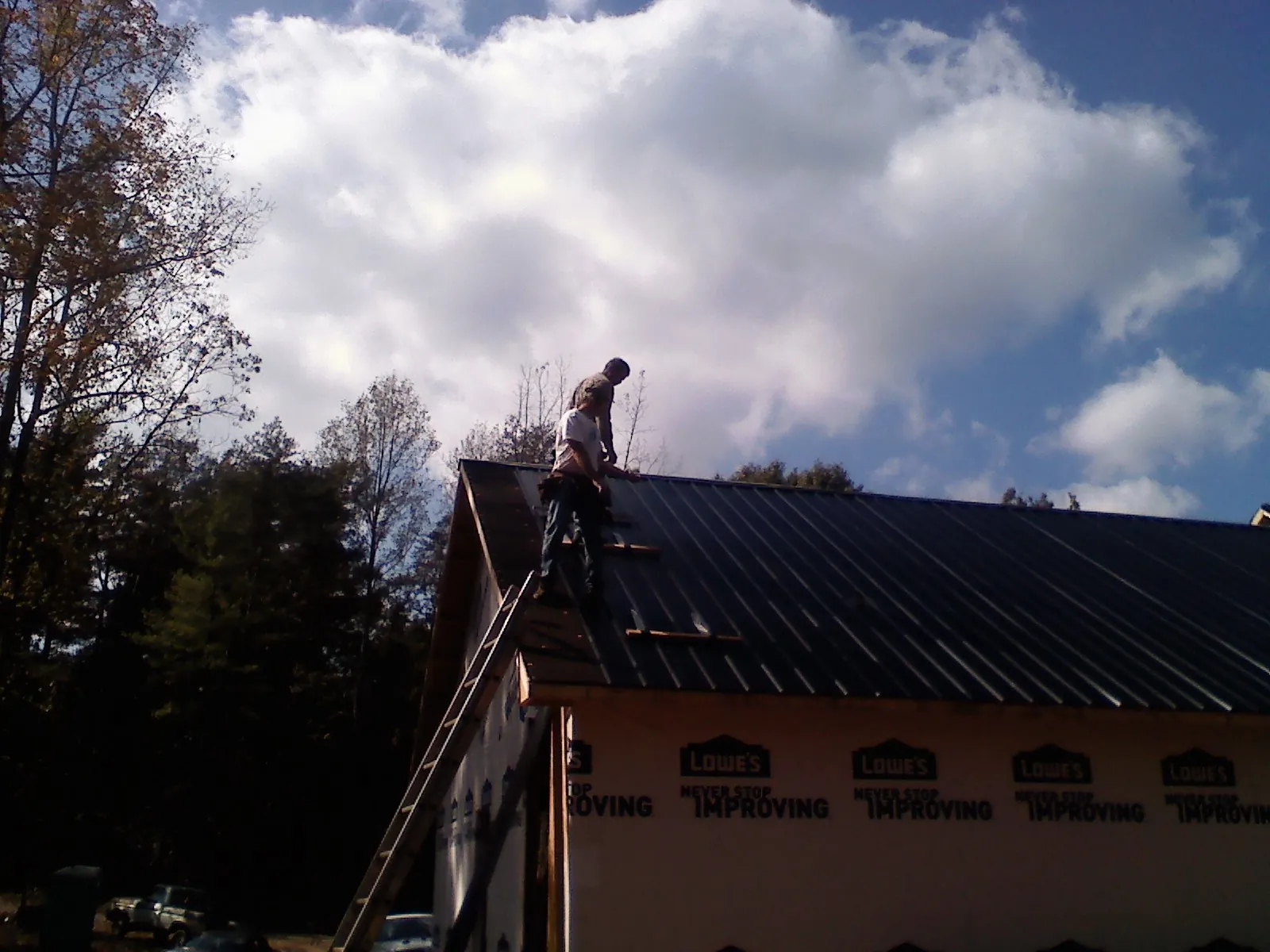 Roofer fastening dark metal panels high against a cloudy sky, from a Roof Inspection job in Romney