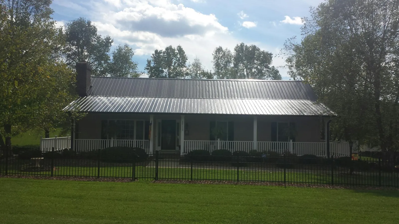 Gray metal roof on a brick ranch with a full width front porch — Gutter Guard Installation work by our crew in Romney