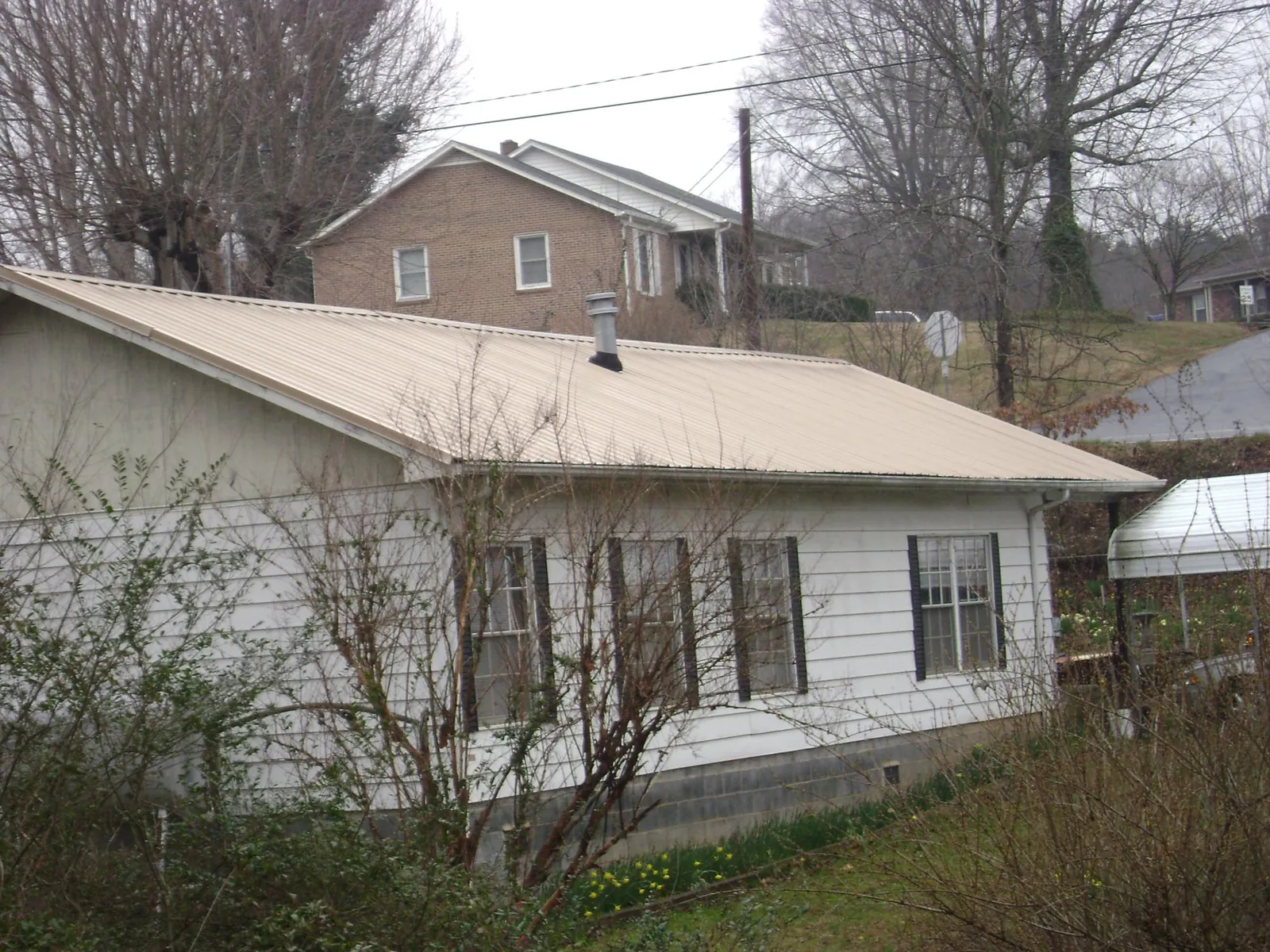 Tan metal roof on a white sided house set into a hillside — Commercial Roofing by Roofing Brothers in Romney