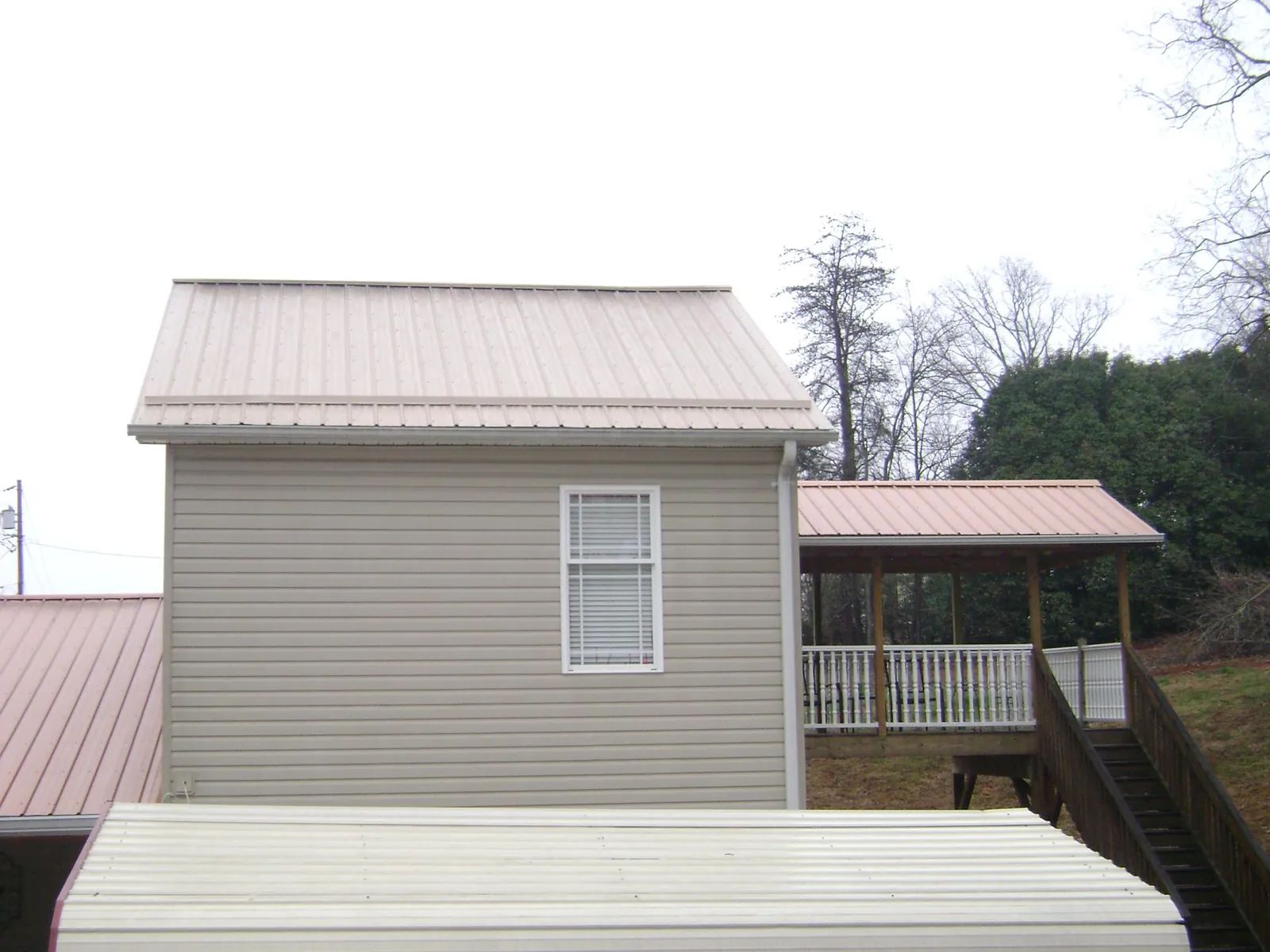 Tan metal roofs on a two story addition and attached porch, from a Roof Replacement job in Romney